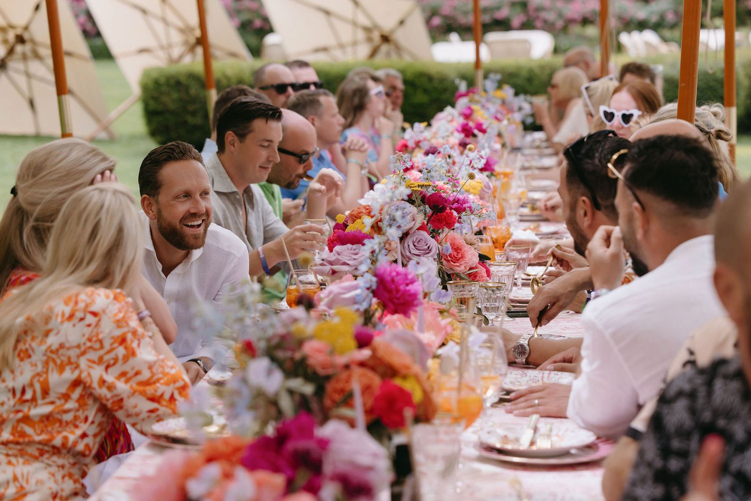 A festive outdoor wedding reception with colorful floral centerpieces and guests enjoying a meal.