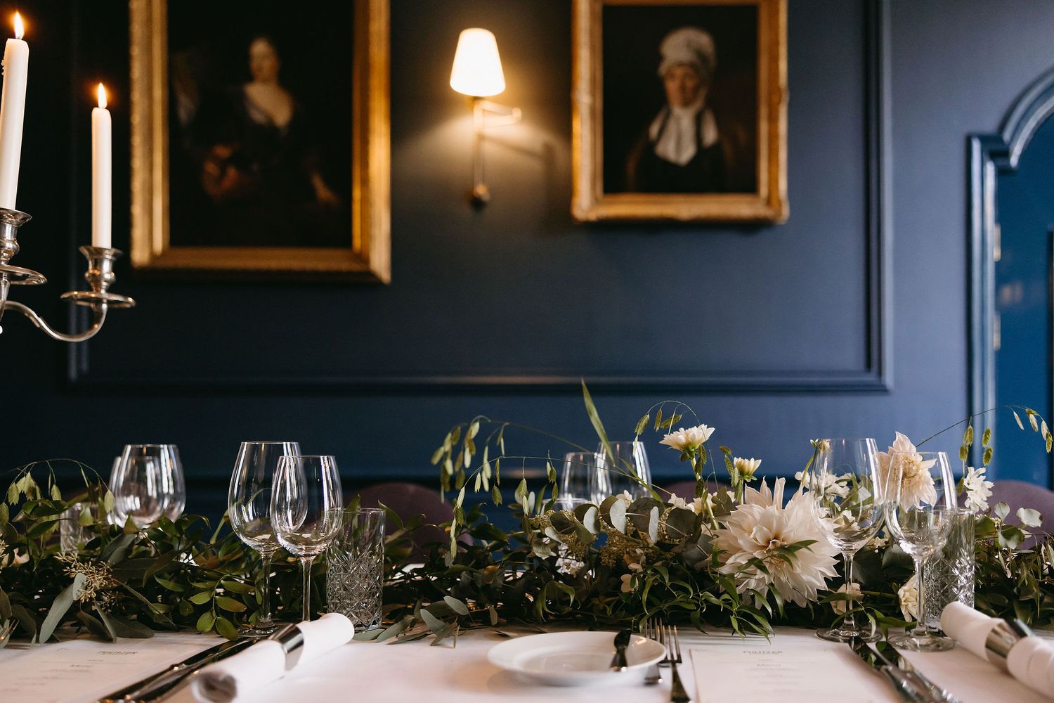 Wedding reception table decorated with white floral arrangements and candles against dark blue walls.