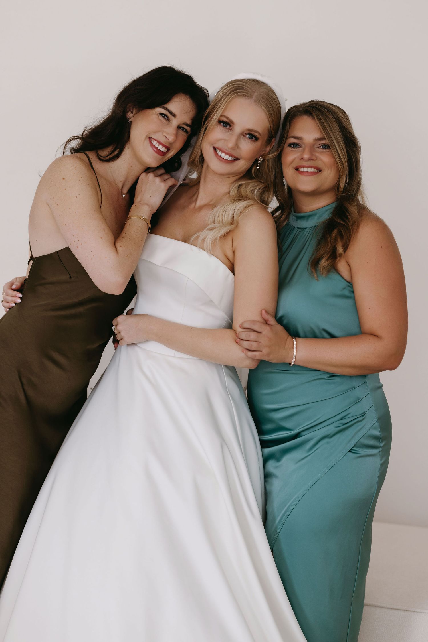 Three women in elegant dresses smiling together at a special occasion.
