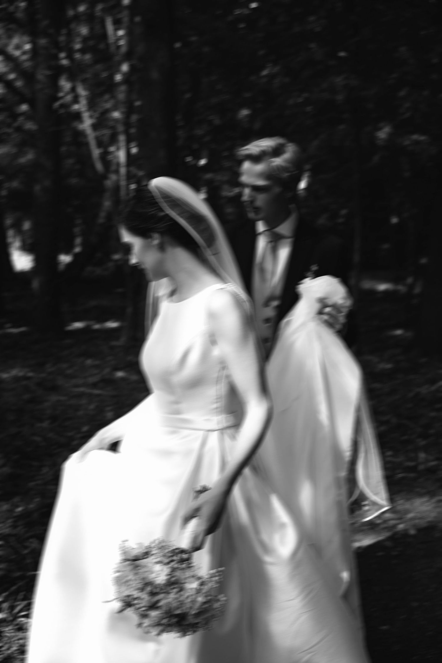 Motion-blurred figures in white dresses walk along a wooded path creating an ethereal effect.