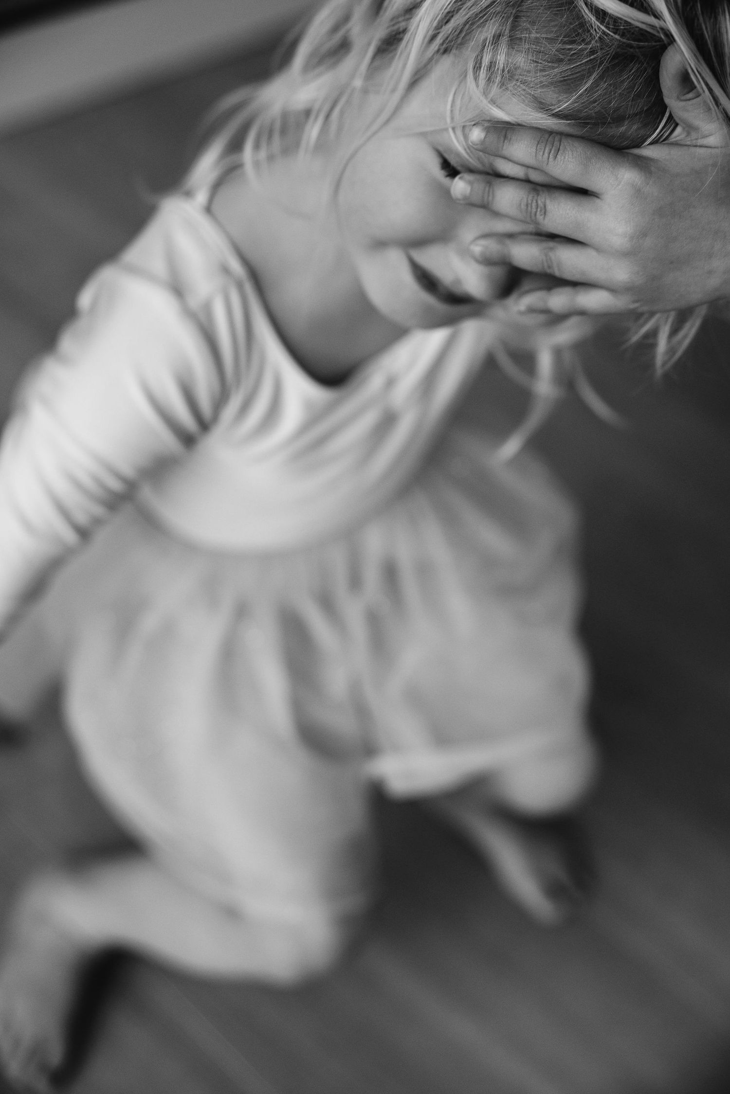 An artistic black and white portrait of a child covering their face while looking down.