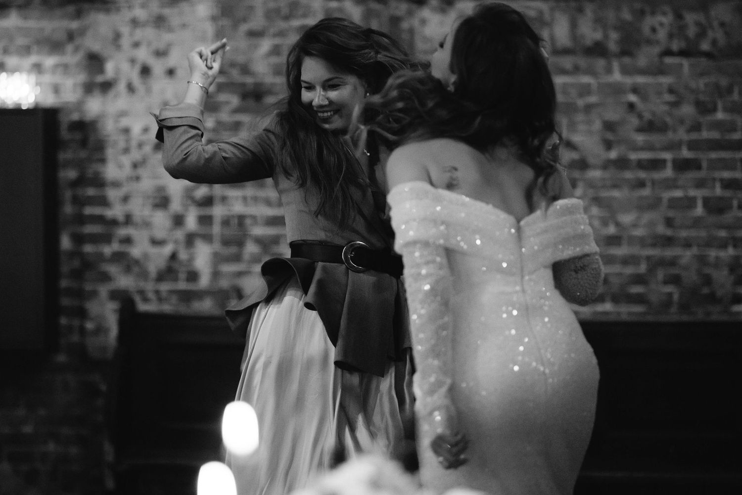 Dancing celebration at wedding reception with sparkly dress against brick wall backdrop.