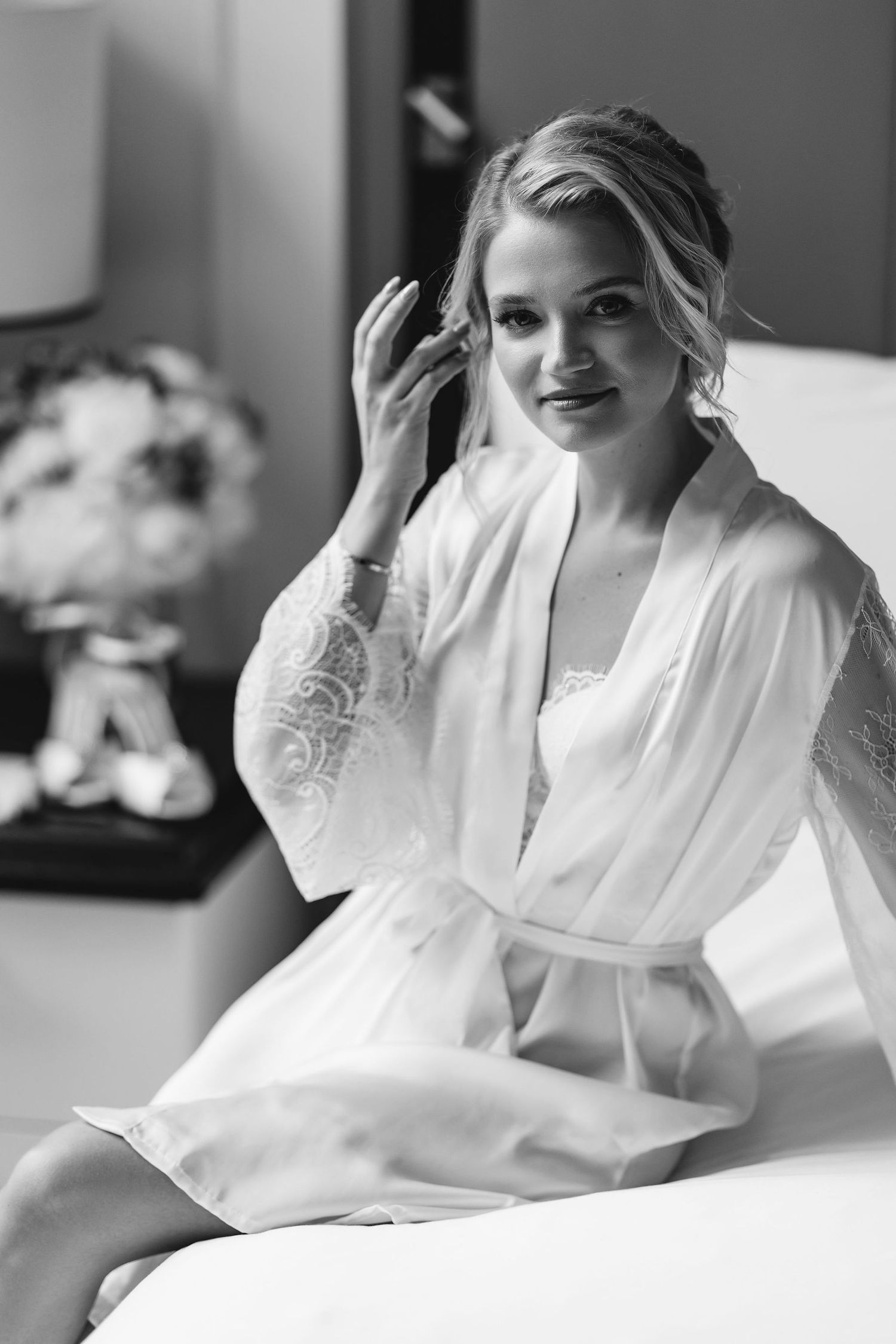 Bride in white robe relaxing on bed during morning preparations.