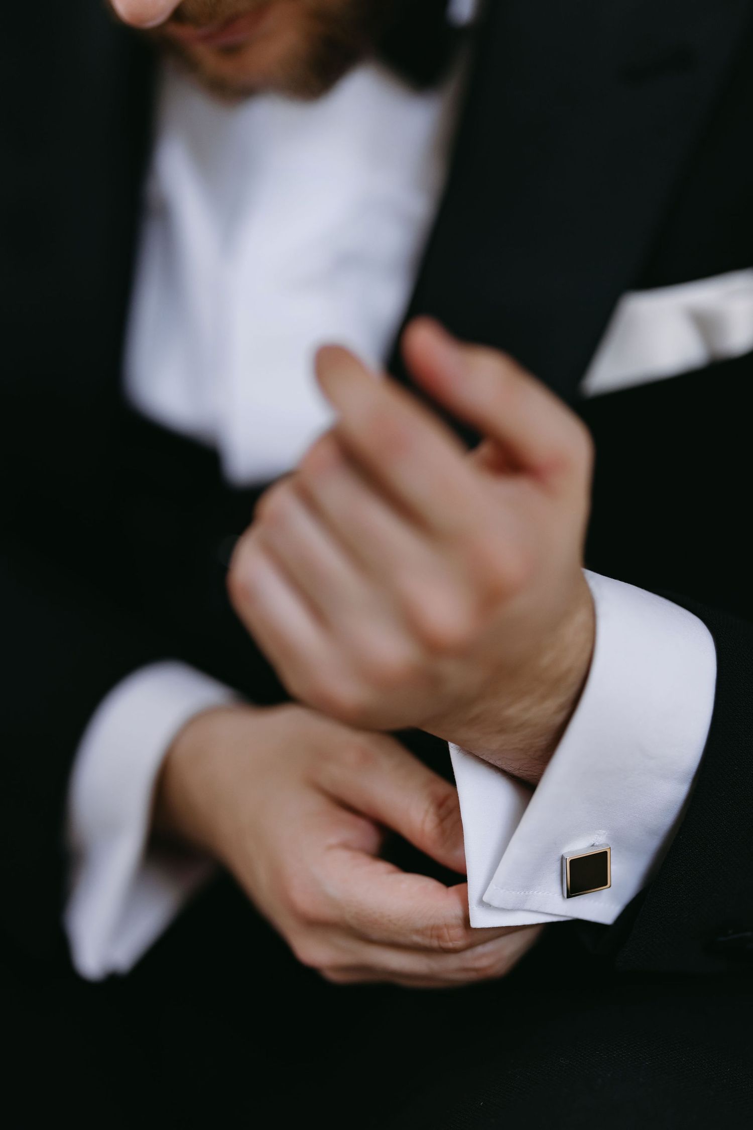 Close-up of hands adjusting formal white cufflinks on a tuxedo sleeve.