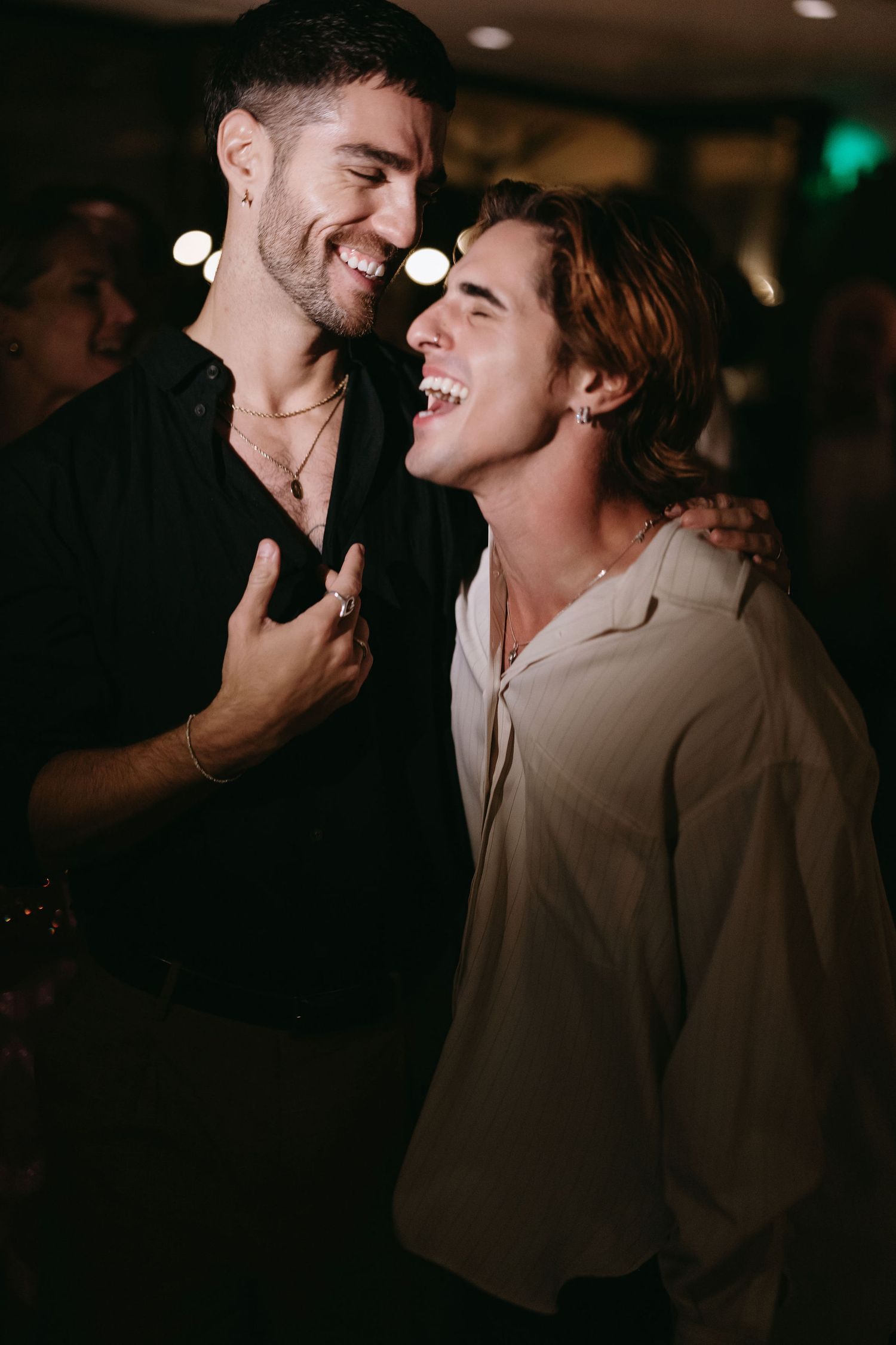 Two friends sharing a joyful laugh together at a dimly lit indoor event.