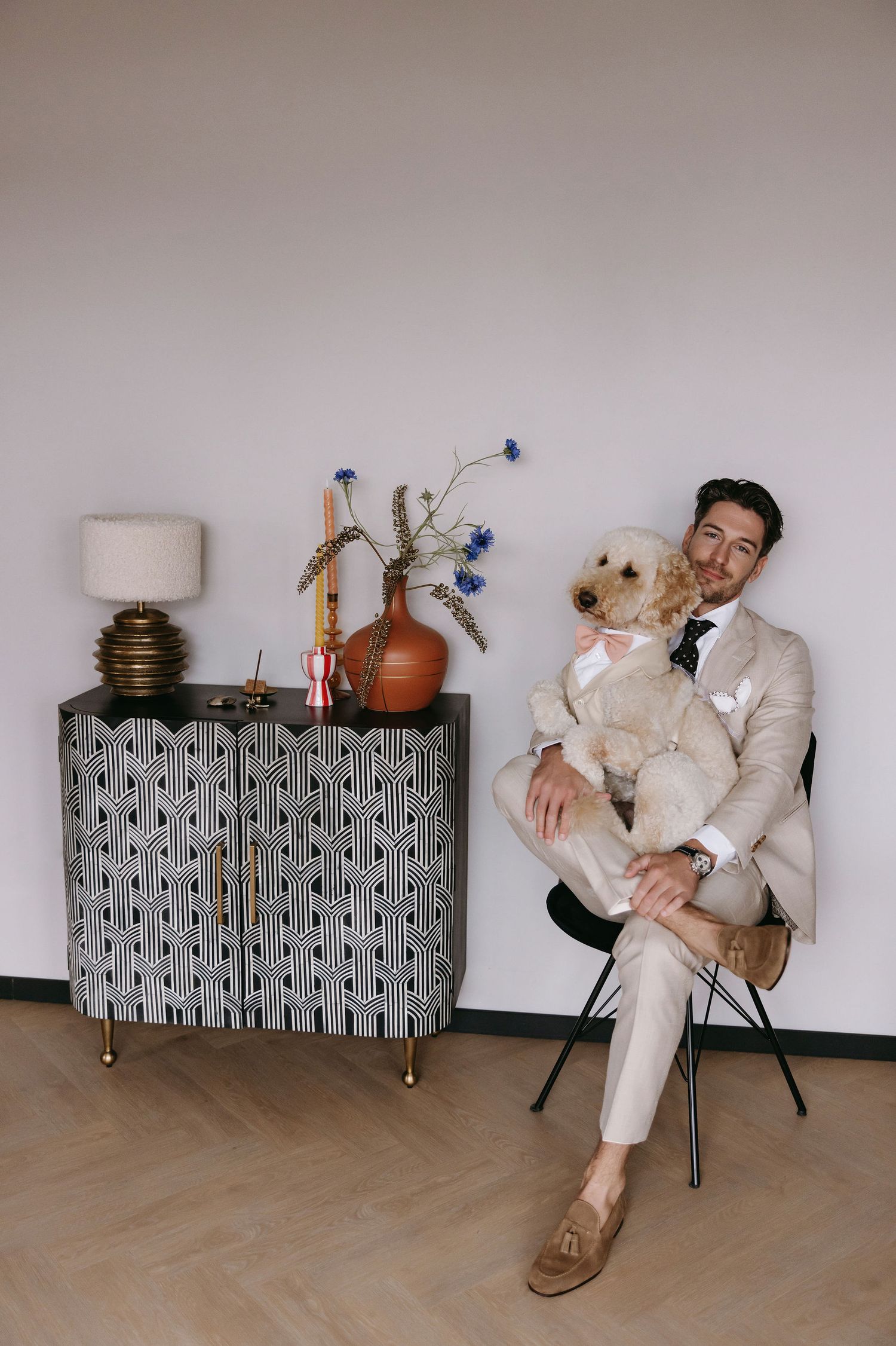 Stylish gentleman in beige suit poses with golden retriever dog beside modern decor.