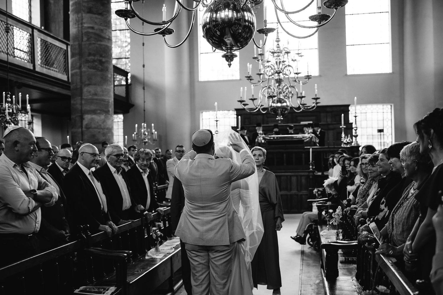A couple embraces during their wedding ceremony in a historic church with ornate chandeliers.