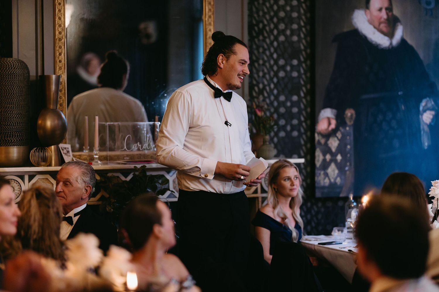 Wedding reception scene with guests and servers in a dimly lit elegant dining room.