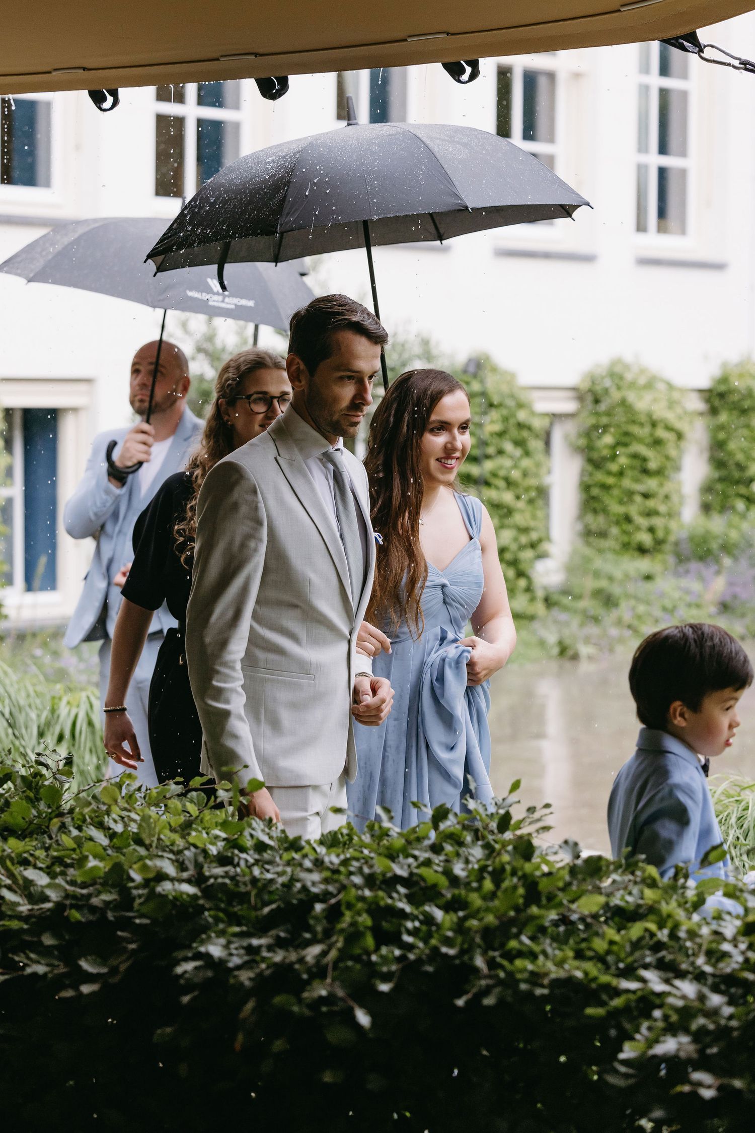 Wedding party guests with umbrellas walking outside venue on rainy day.