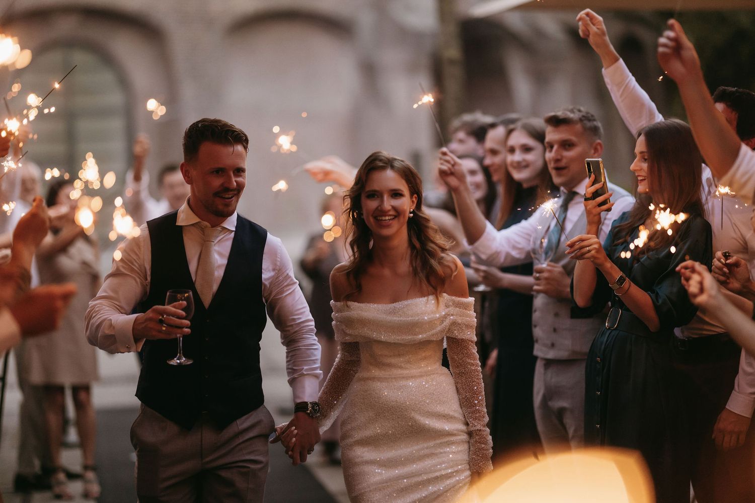 Wedding couple walking through sparkler exit with celebrating guests at night.