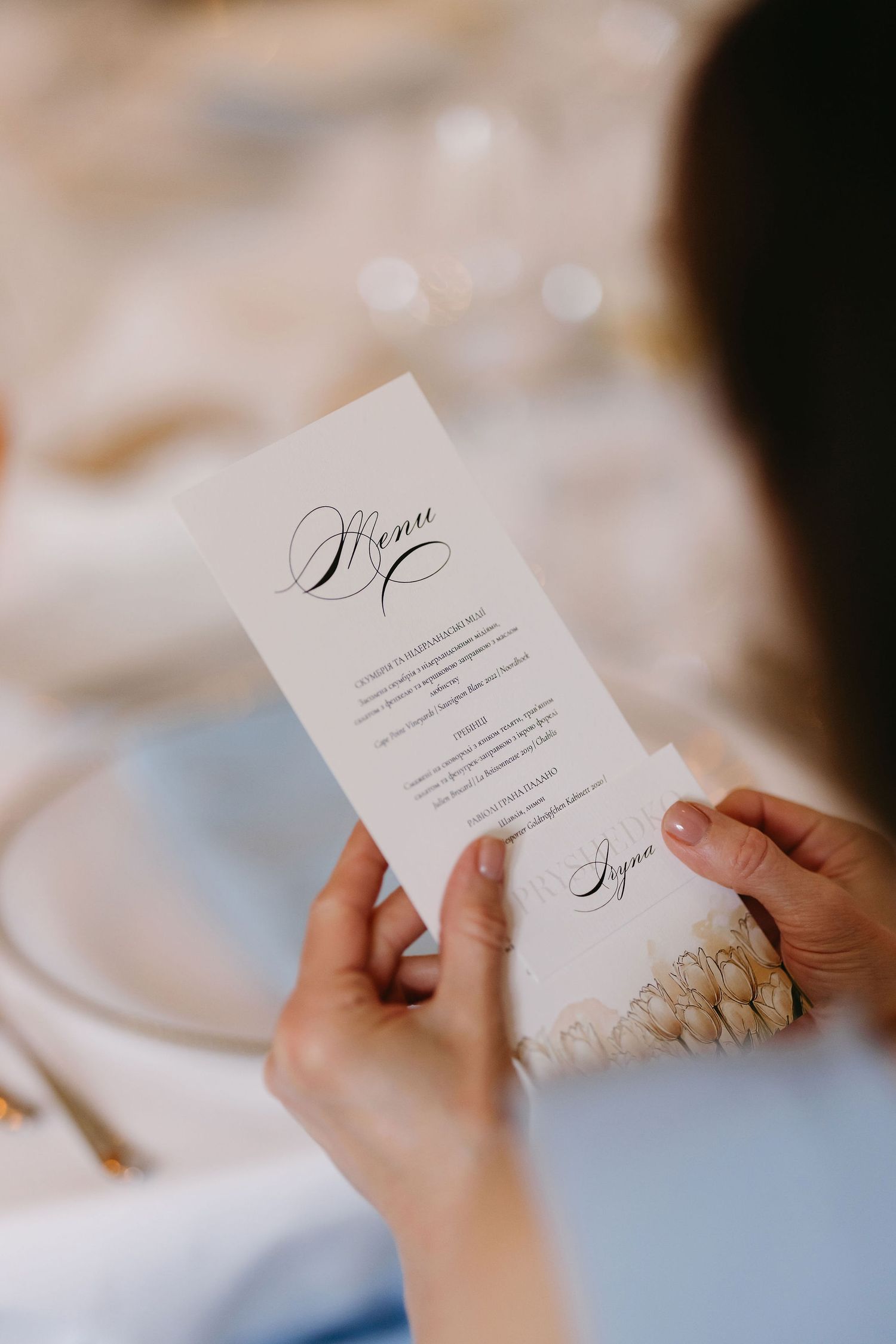 Elegant wedding menu or program card held in hands against a soft blurred background.