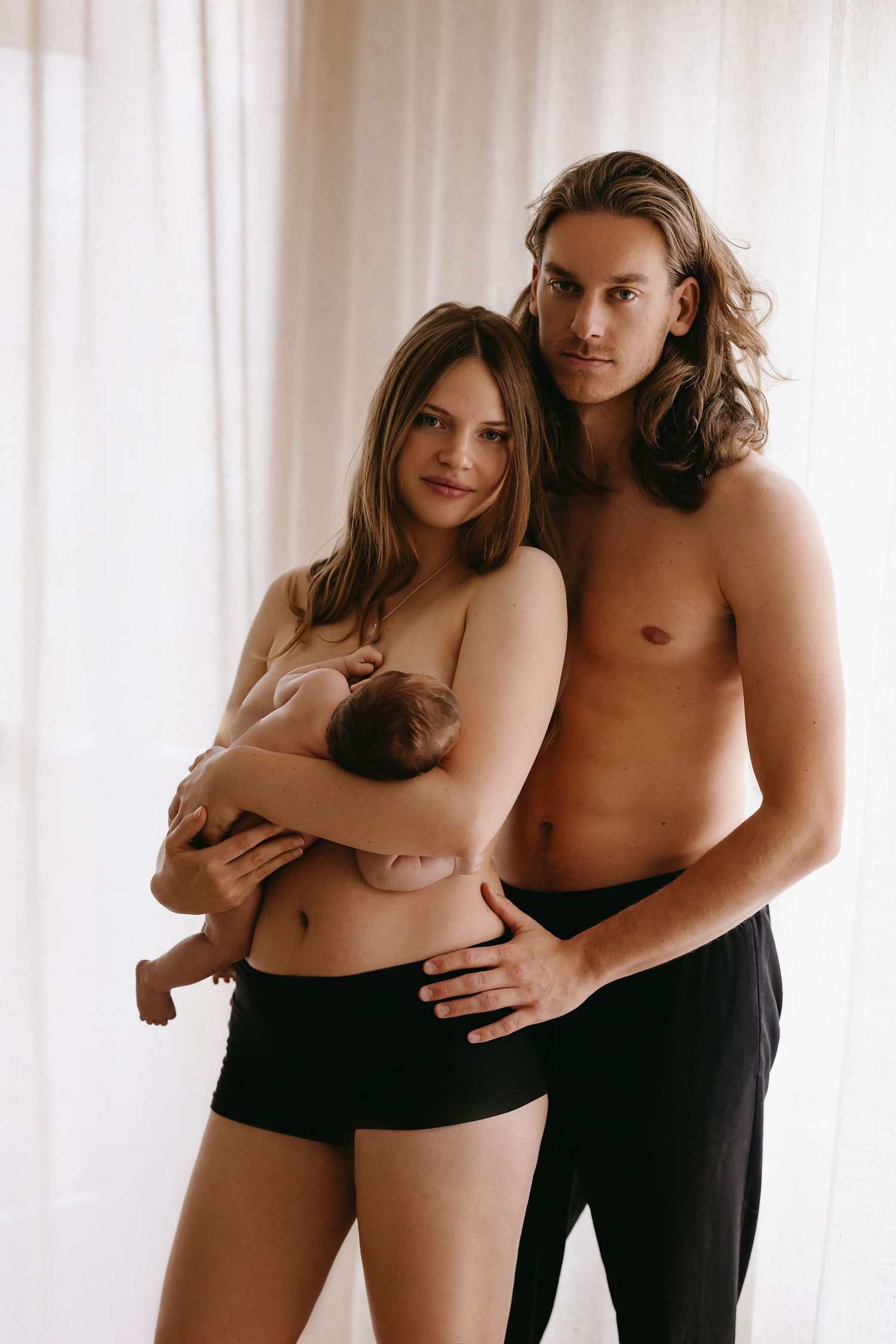Sensual artistic photo series of couple in black and white, shot against white curtained backdrop.
