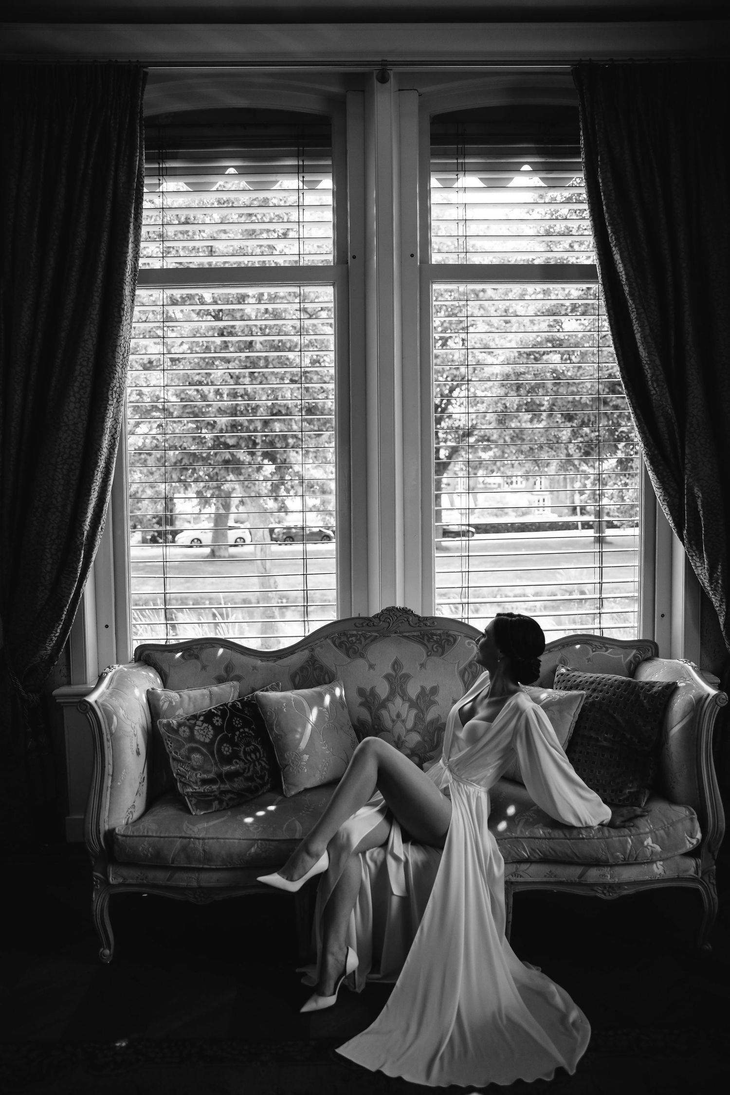 A sequence of black and white photos showing a flowing white dress against a cozy window seat with dark curtains.