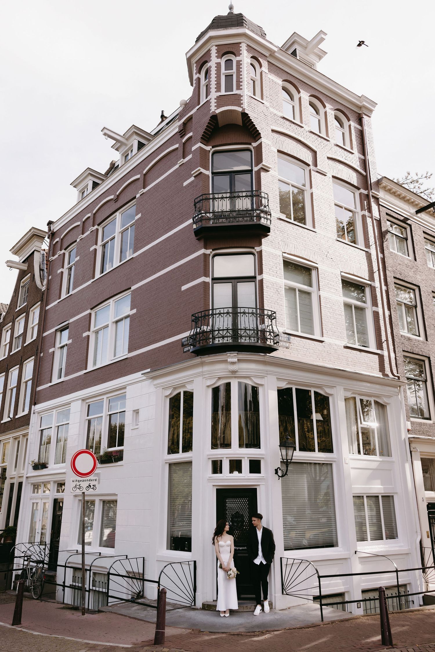 Classic Amsterdam corner building with ornate architecture and balconies stands elegantly at an intersection.