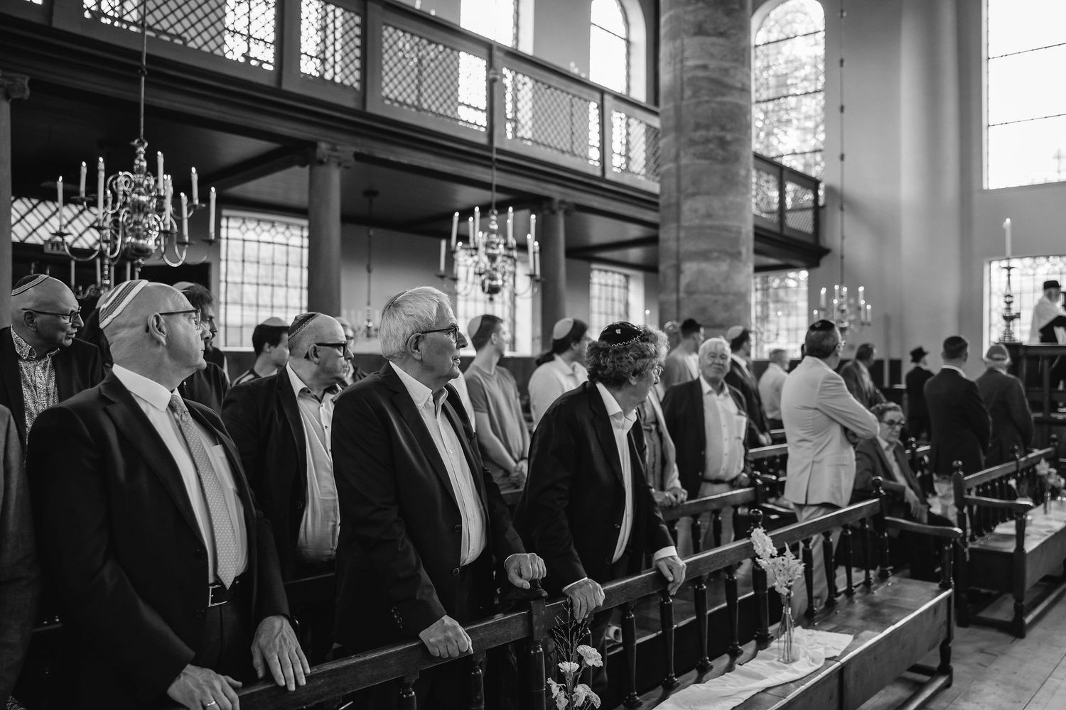 Row of guests standing in formal attire inside a church with high windows.