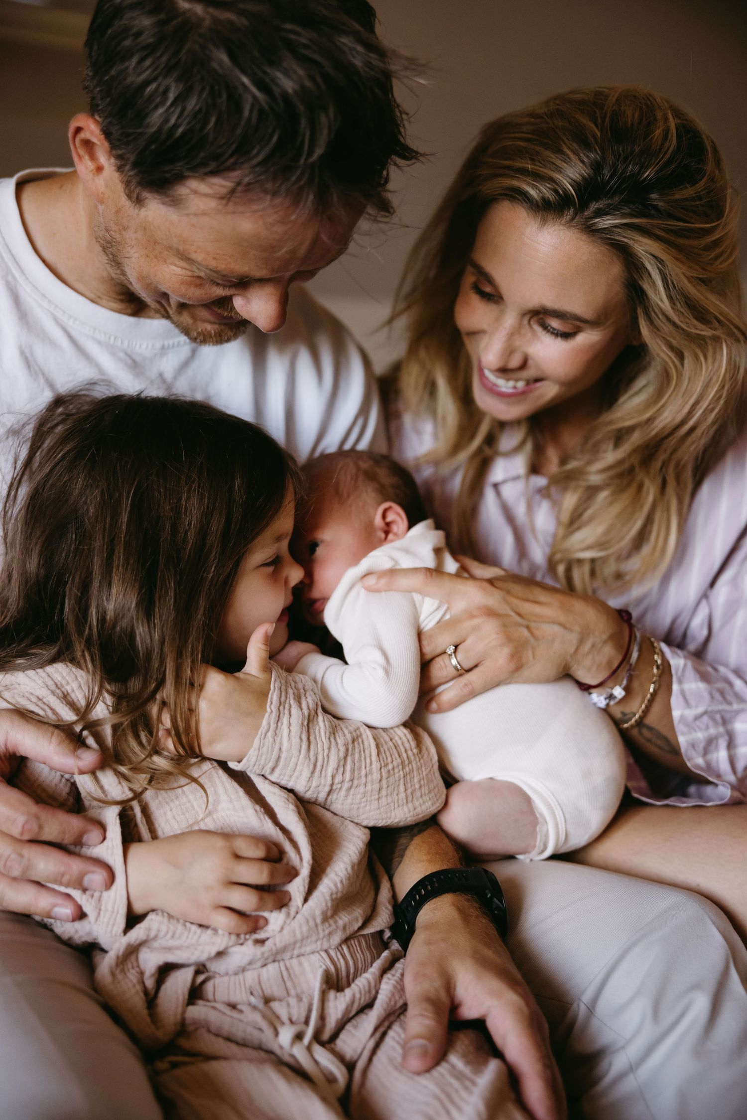 Intimate family moments captured in warm tones on comfortable bedding.
