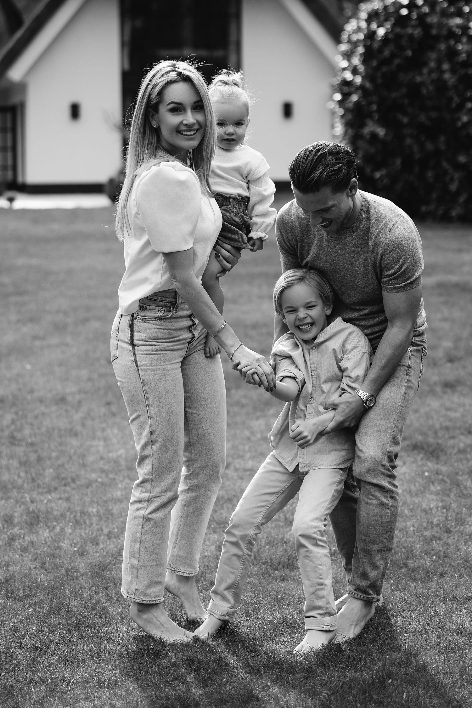 A candid black and white family portrait outdoors with two children playing in front of a white house.