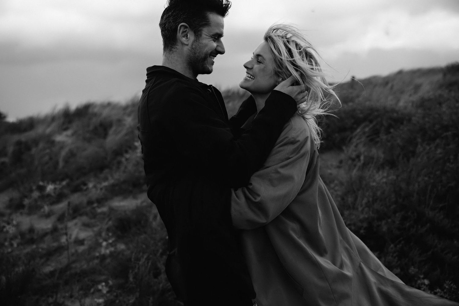 Romantic black and white portrait of couple embracing on hillside.