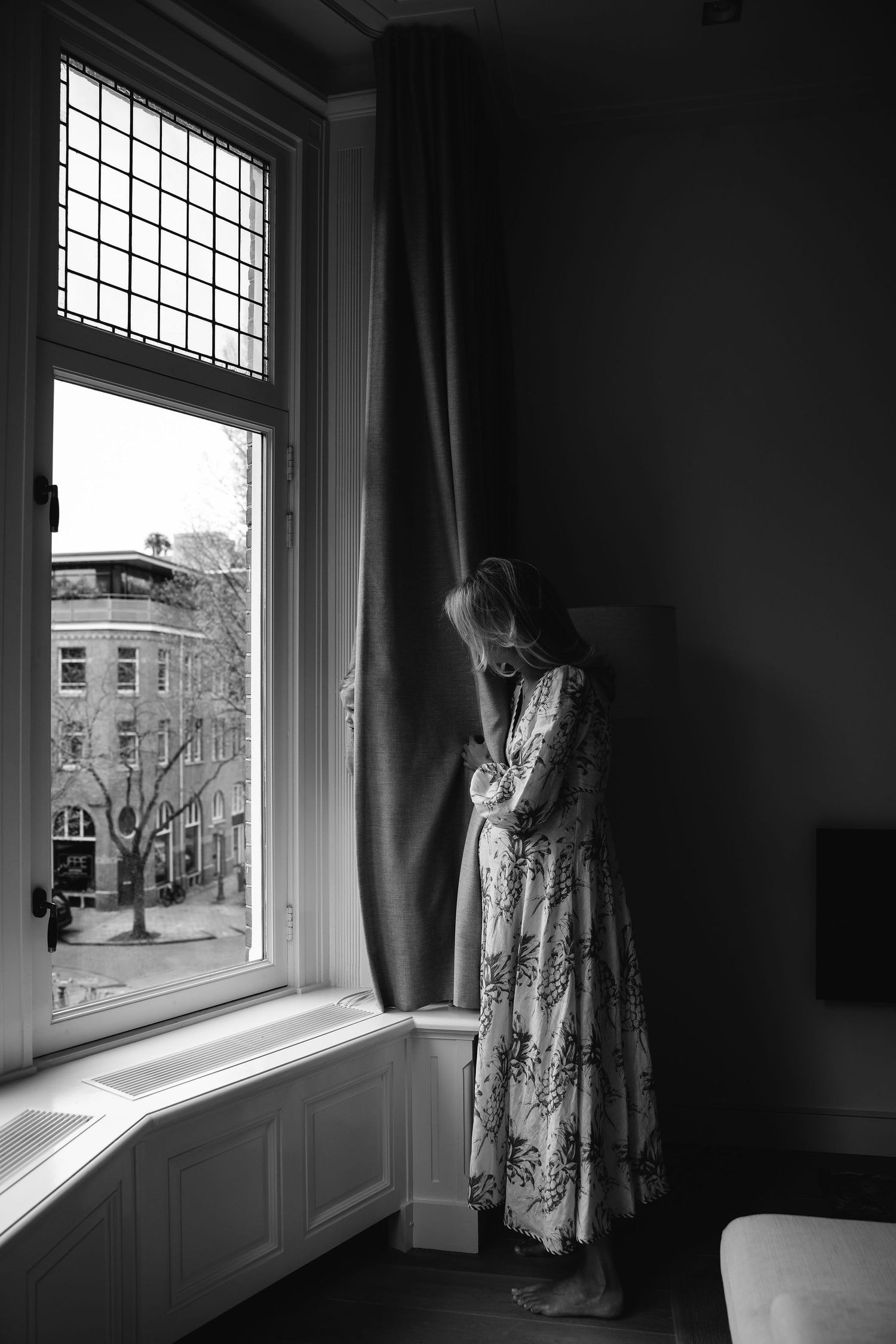 Atmospheric black and white silhouette by window with city buildings visible.