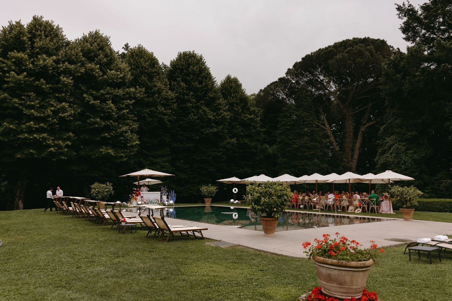 Pool area with lounge chairs and umbrellas set up in a garden setting.
