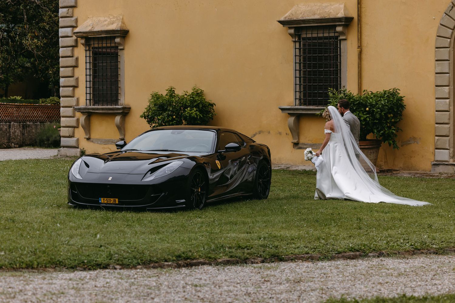 Black Ferrari parked on grass beside elegant wedding scene at Italian villa.