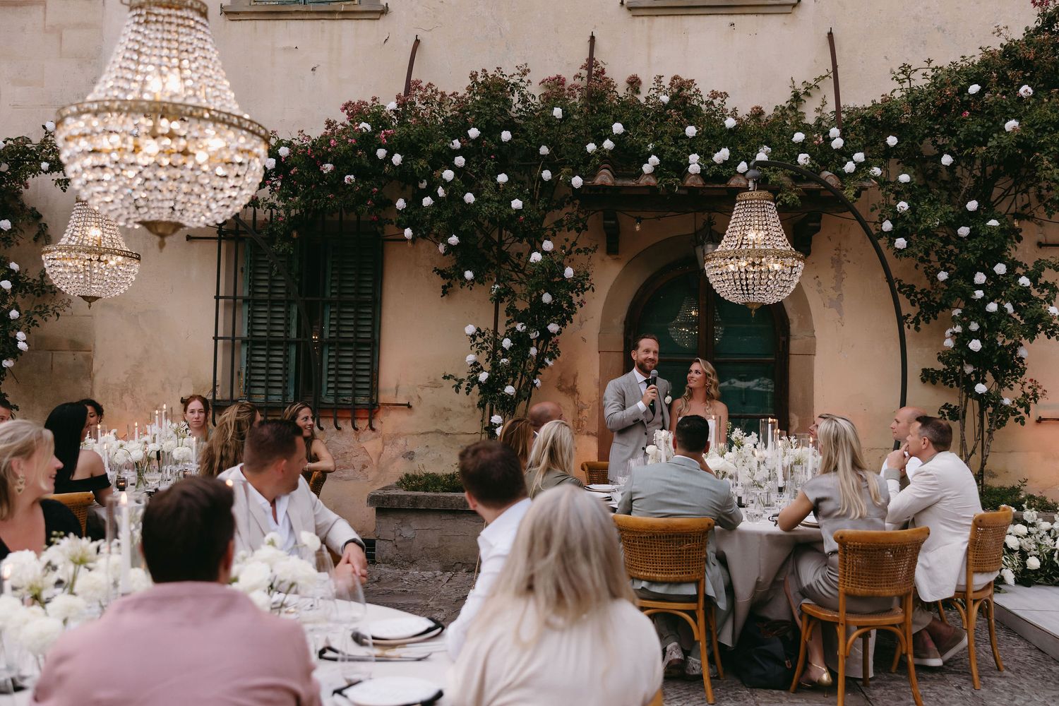 Outdoor wedding reception under crystal chandeliers and floral arch decorations.