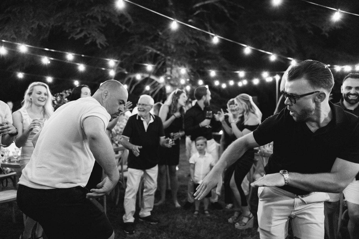 Outdoor wedding reception celebration under string lights at night.