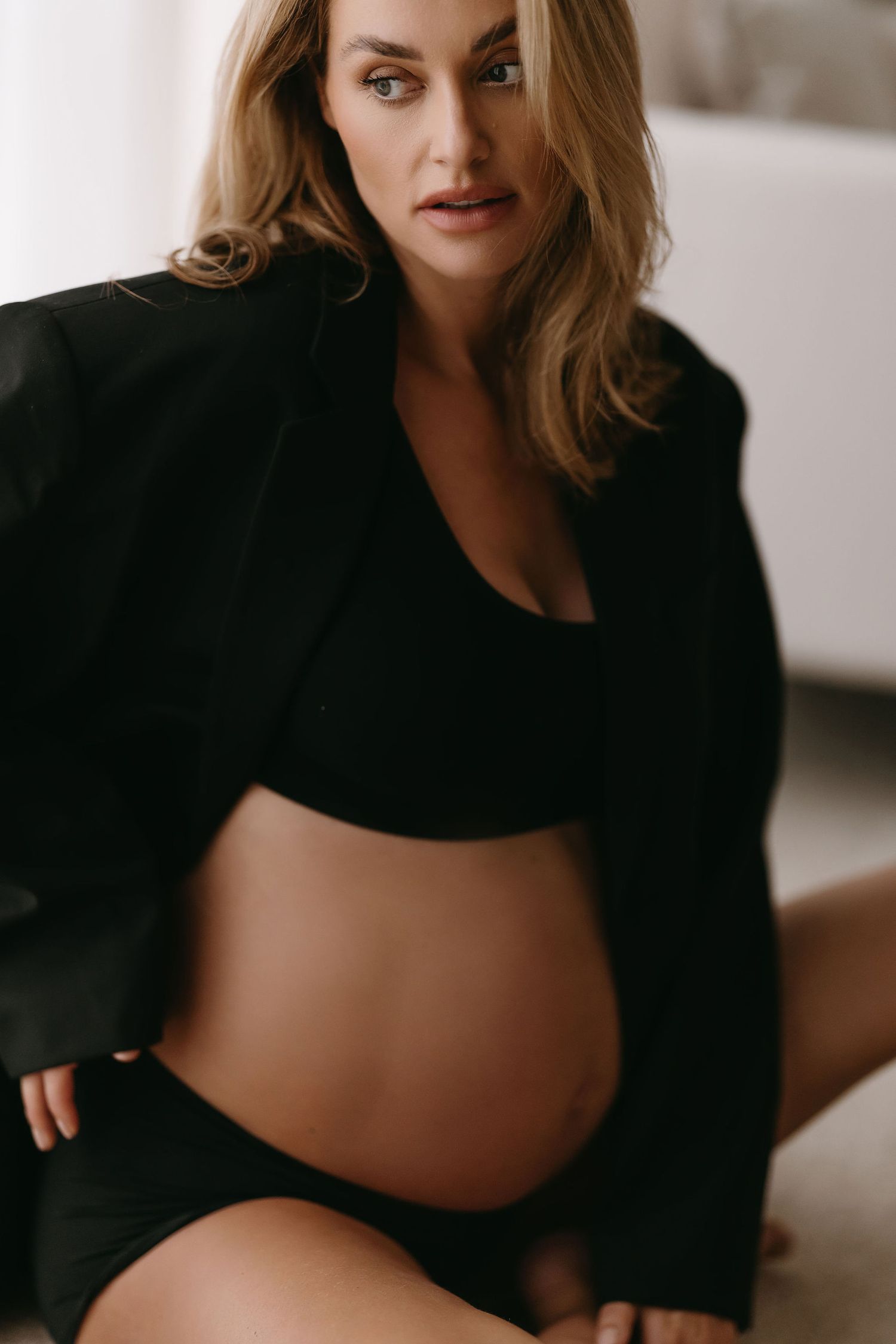 Elegant maternity portrait in black outfit against white backdrop.