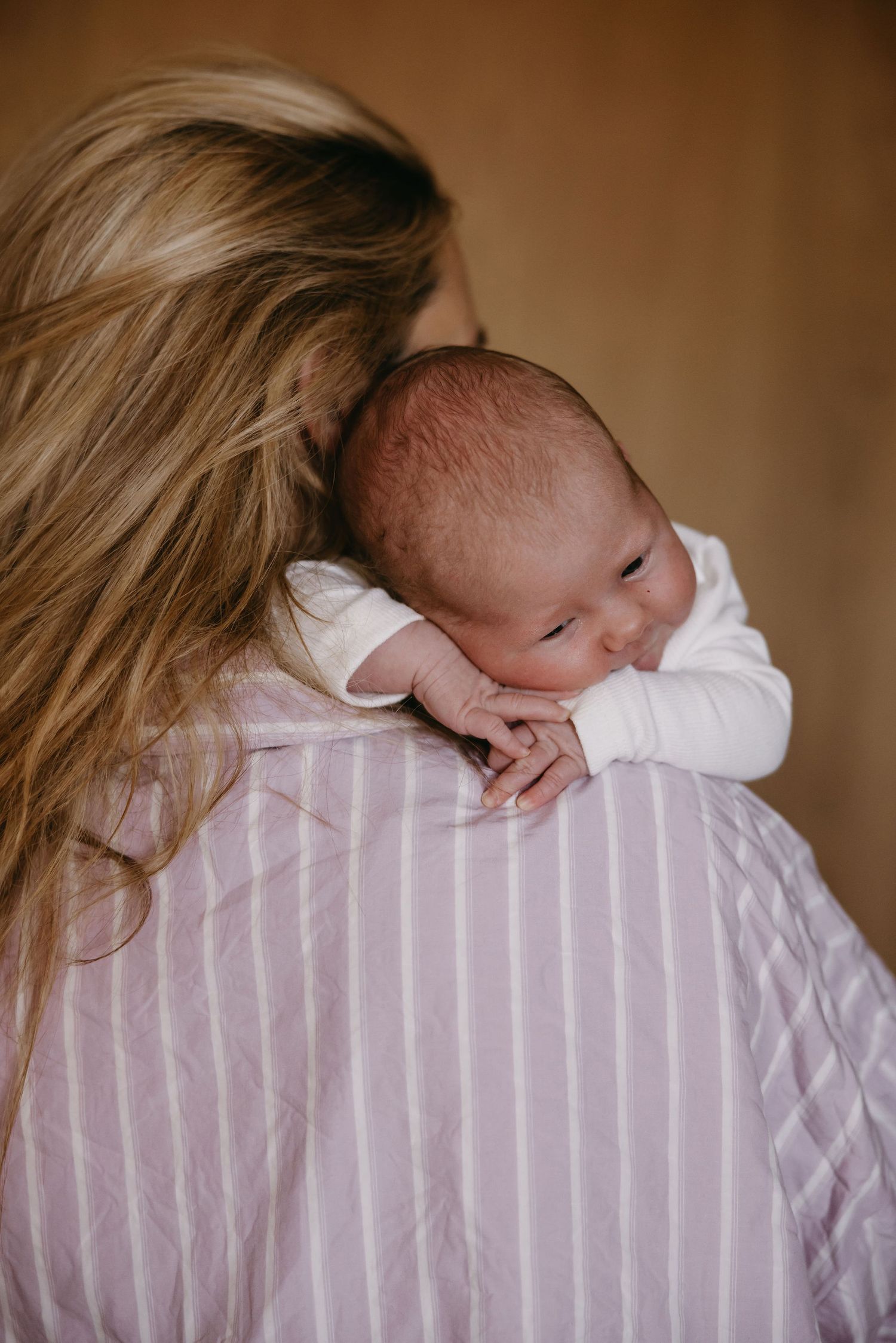 A newborn baby sleeping on a parent's shoulder wearing a pink striped shirt.