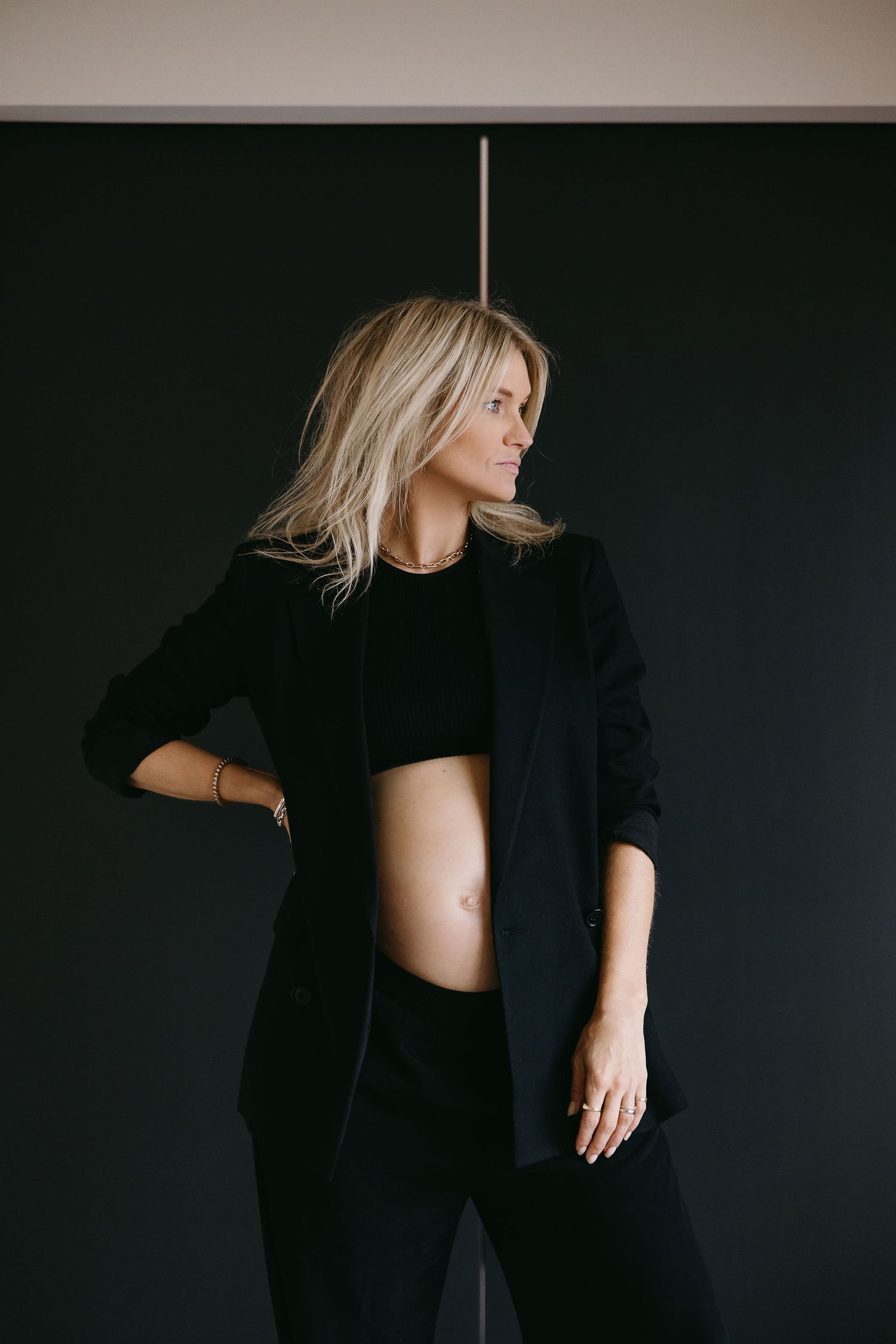 Artistic maternity photoshoot featuring a woman in black against a dark background.