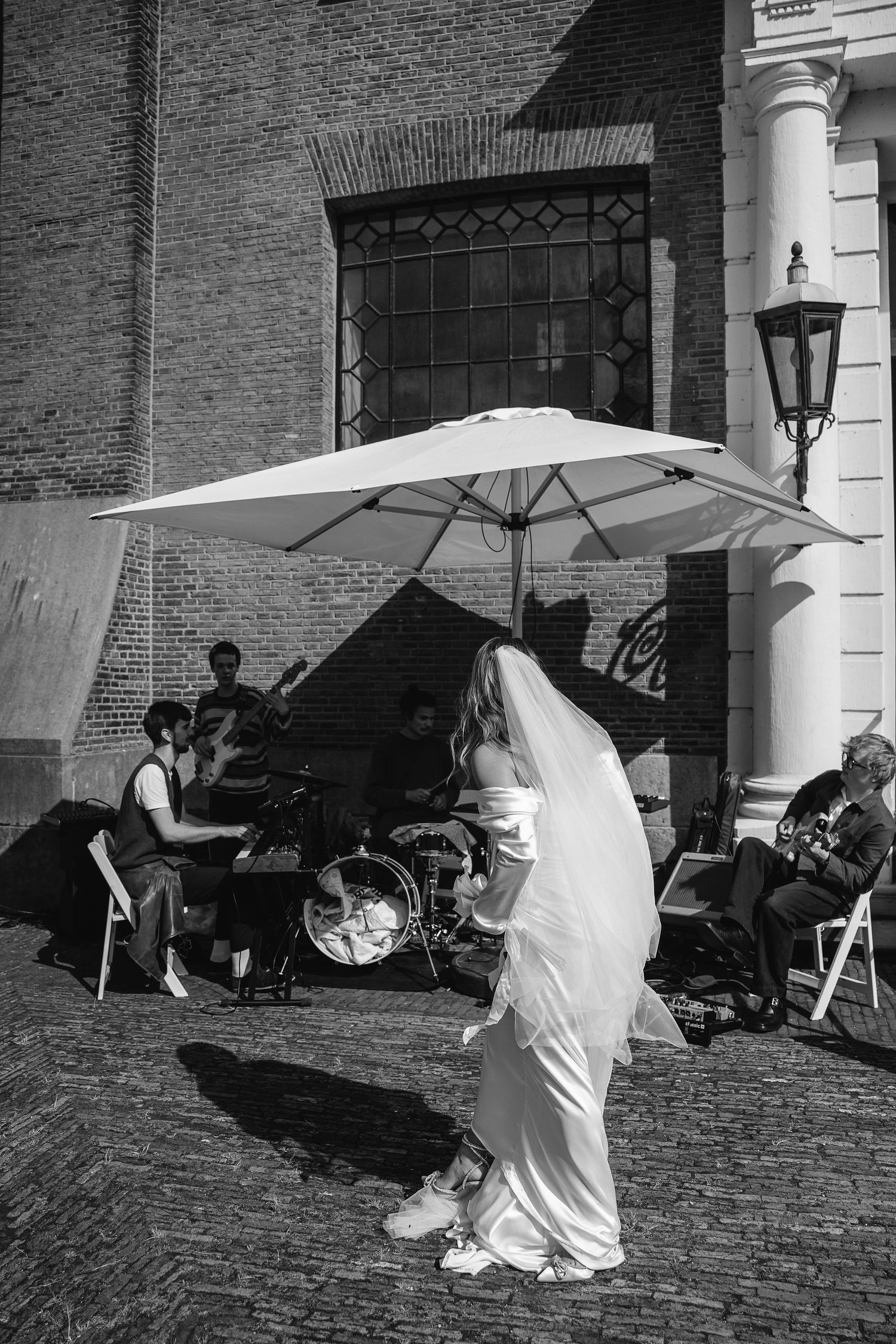 Black and white photo of people with umbrellas outside brick building entrance.