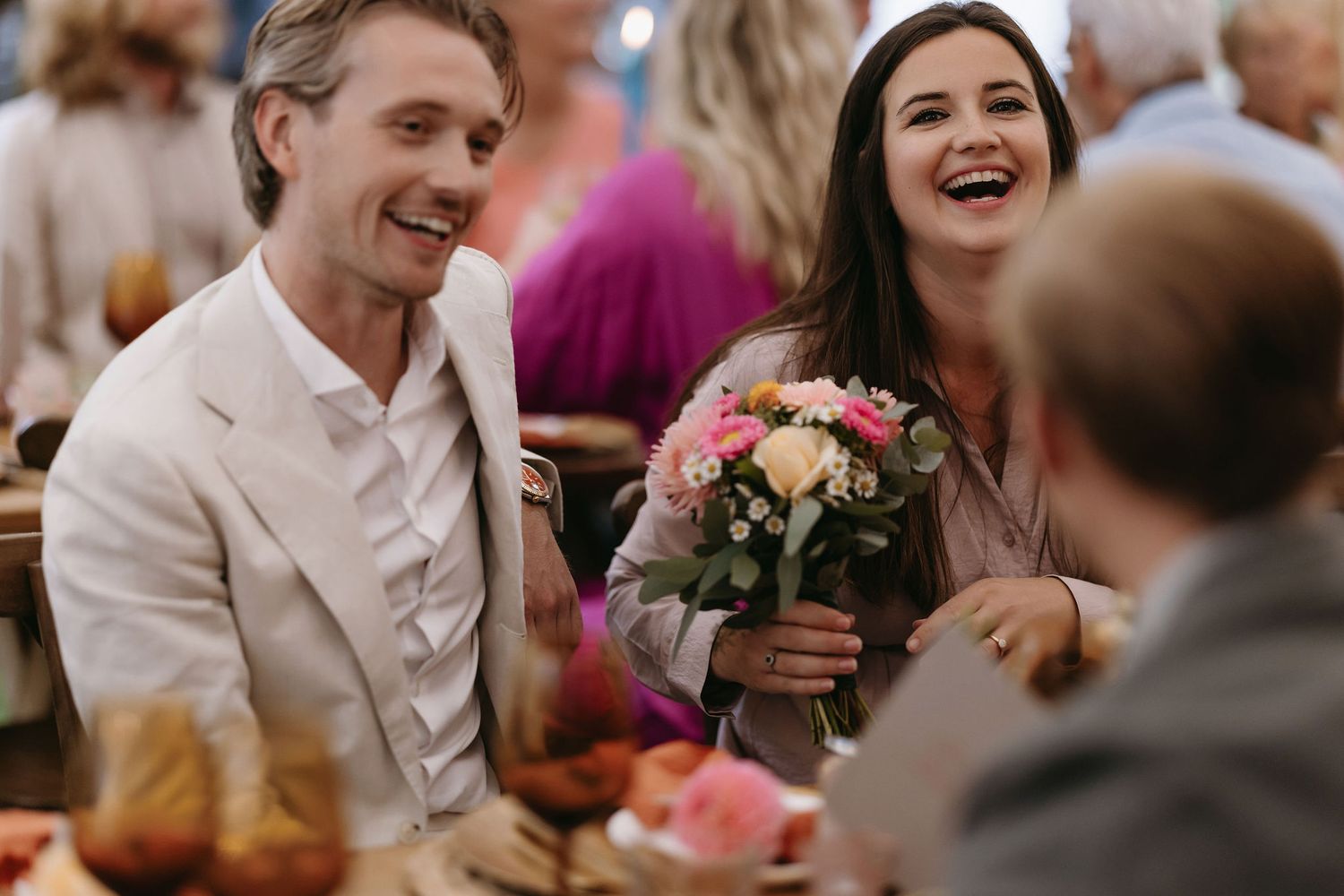 Wedding guests share joyful laughter and celebration during an outdoor reception.
