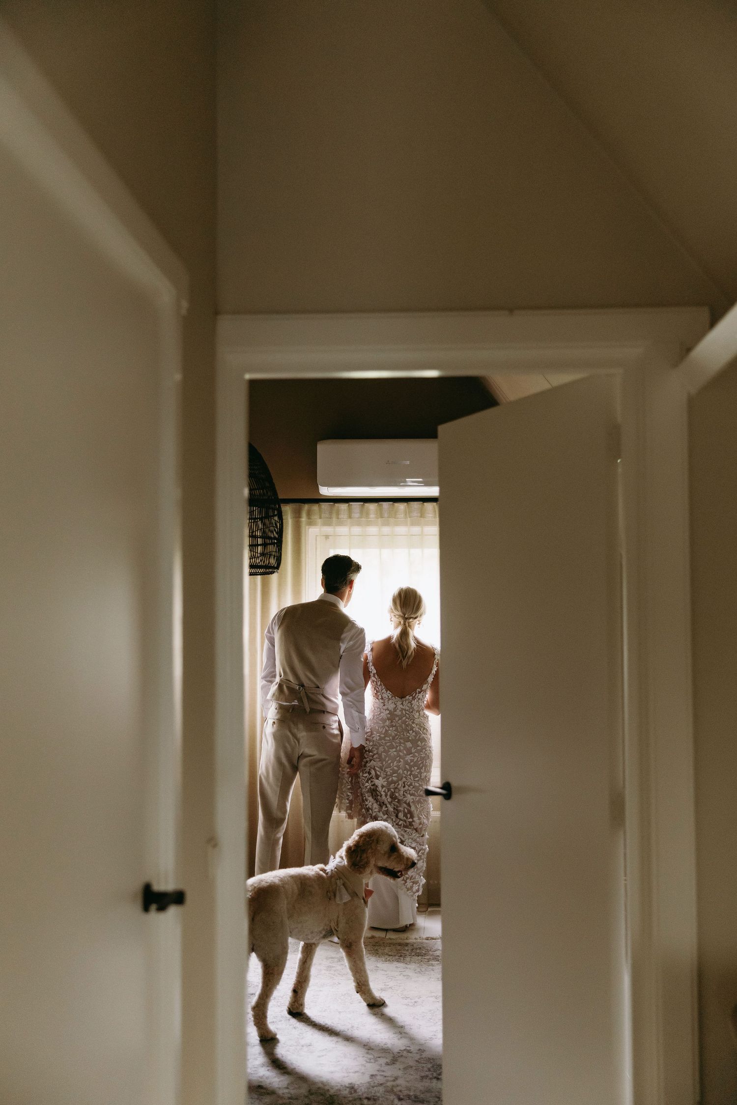 A couple and their dog stand silhouetted in a doorway of a bright interior space.