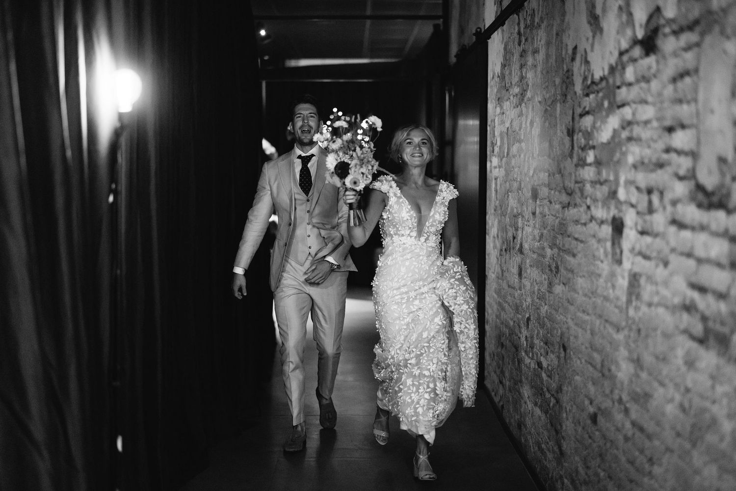 Wedding party walking down a dimly lit hallway with brick walls.