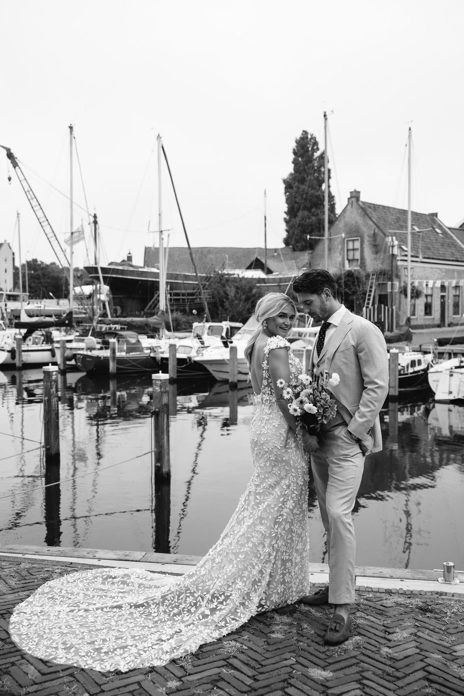 Wedding couple sharing intimate moment by marina with boats and buildings in background.
