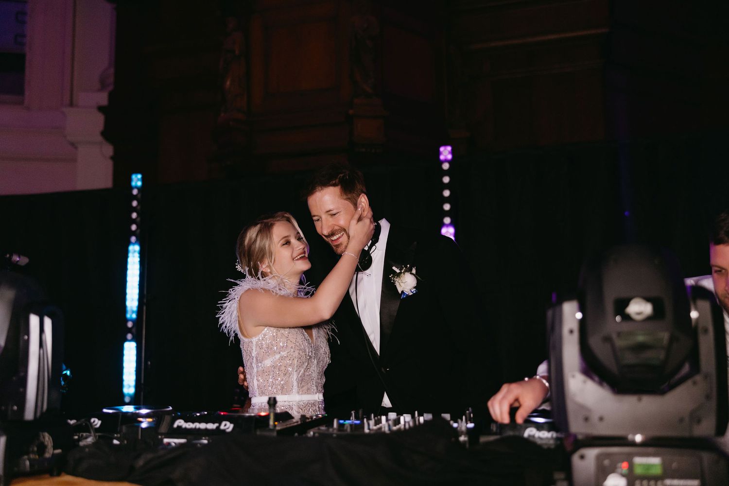 Two people share a tender moment while DJing together with a lighting setup visible in the background.
