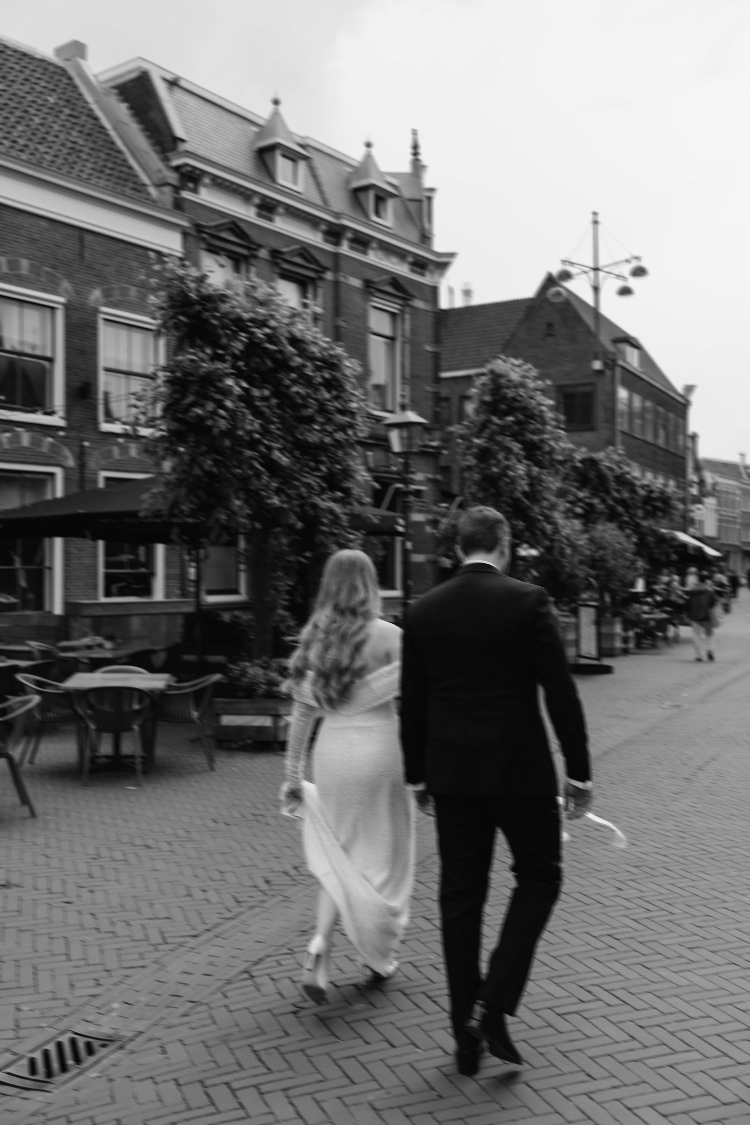 A black and white sequence of images showing a couple walking down a historic cobblestone street with traditional buildings.