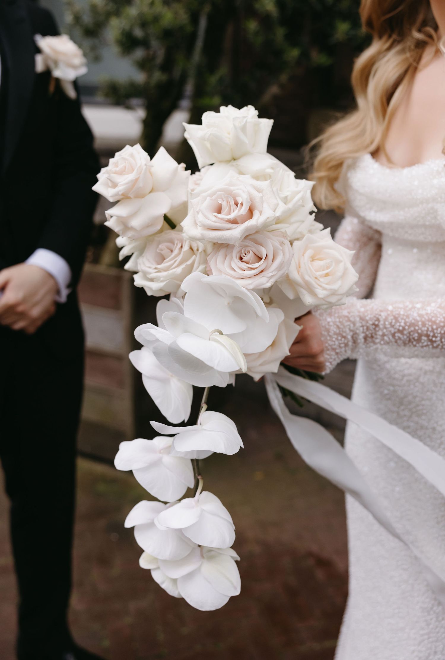 Close-up of delicate white rose and orchid wedding bouquets against a dark background.