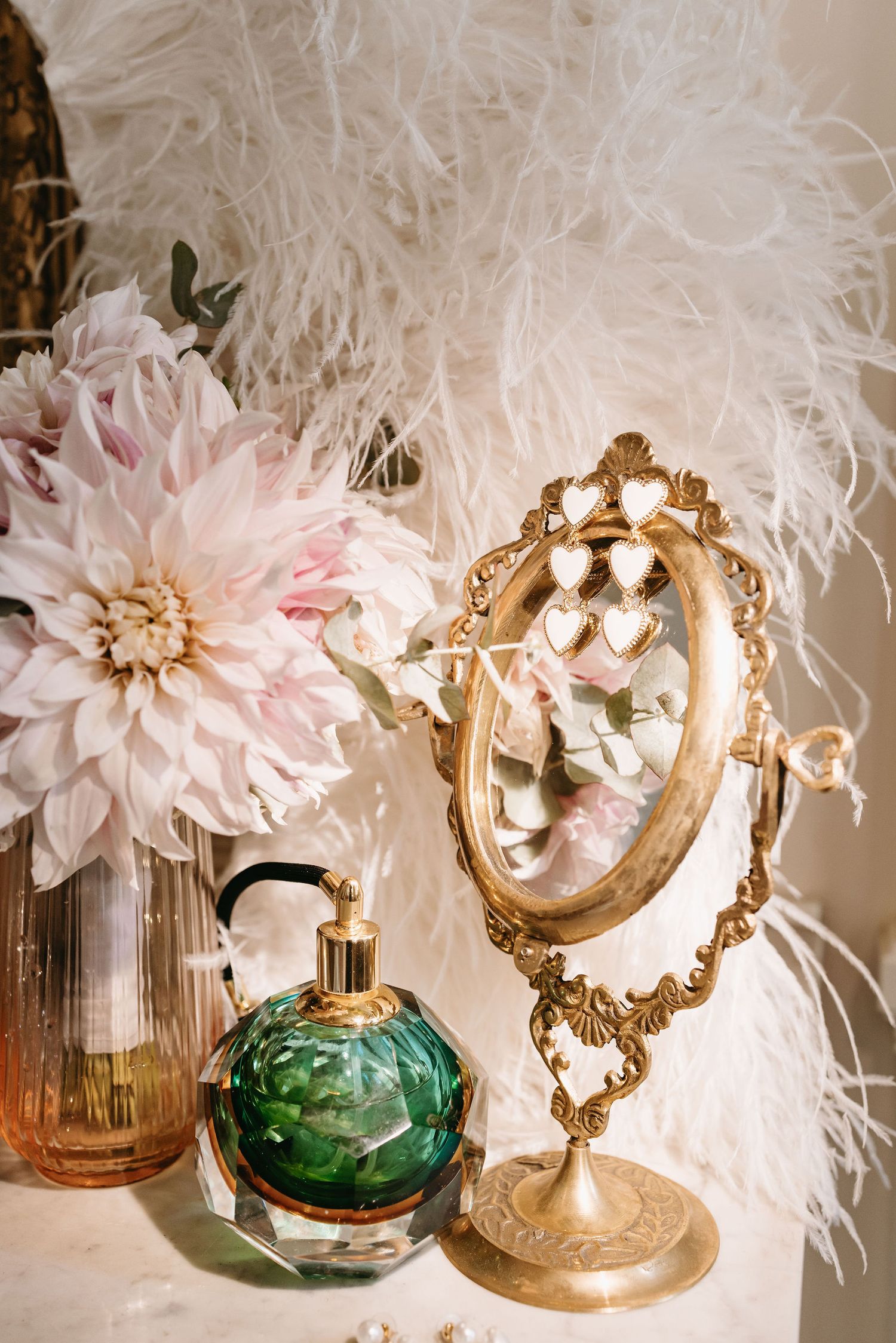 Elegant wedding decor featuring green glass perfume bottles, gold ornate frames, and delicate pink feathers.