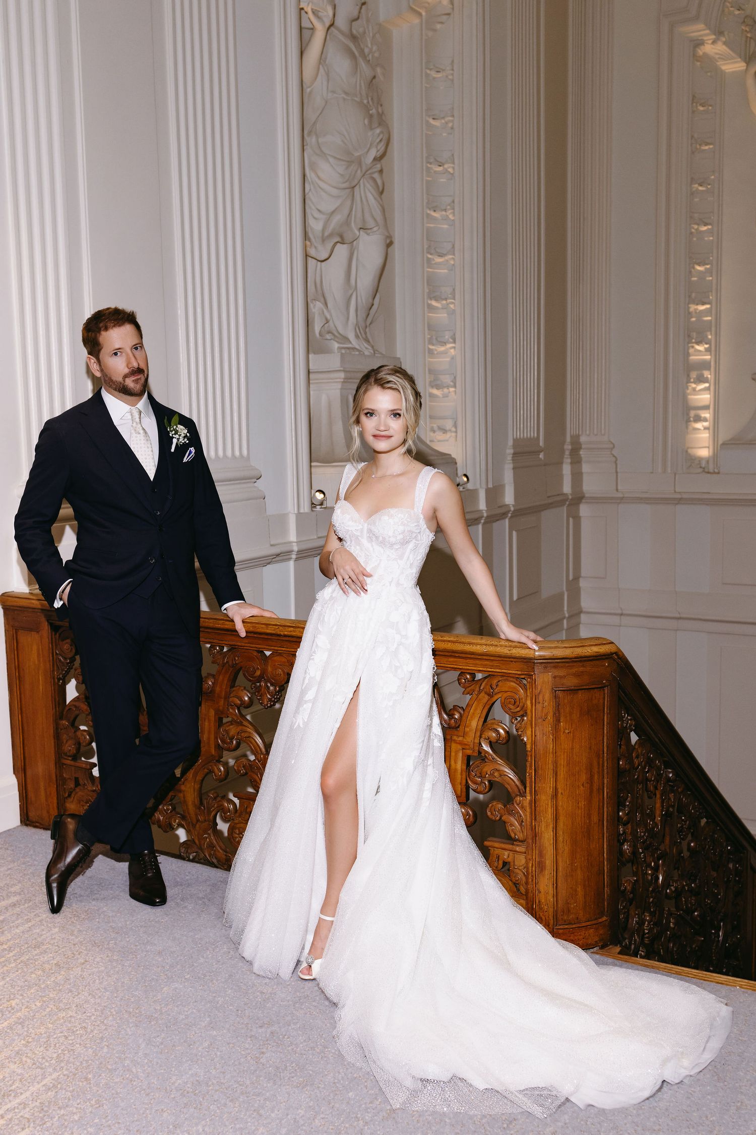 Elegant wedding couple walking through a grand hallway with classical white pillars and ornate woodwork.