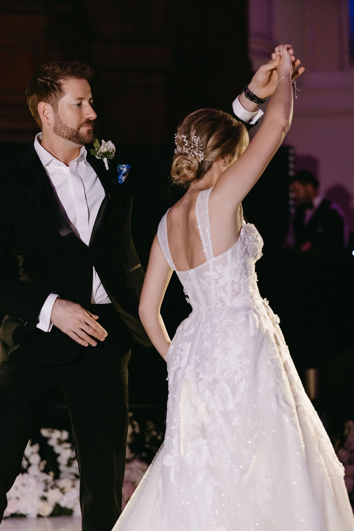 Couple dancing at reception with bride's lace dress twirling in dramatic lighting.