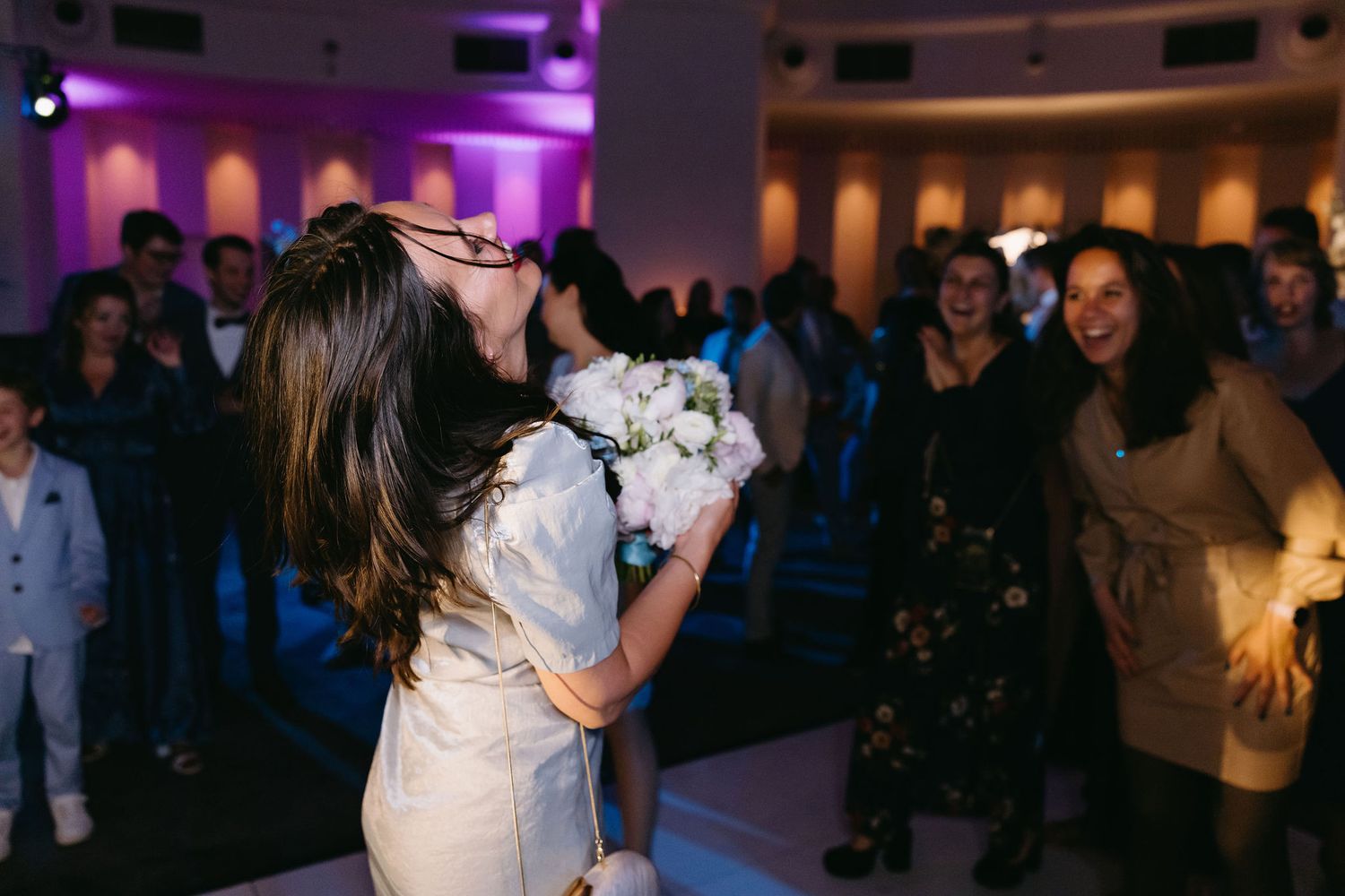 Wedding reception dance floor filled with guests under purple mood lighting.