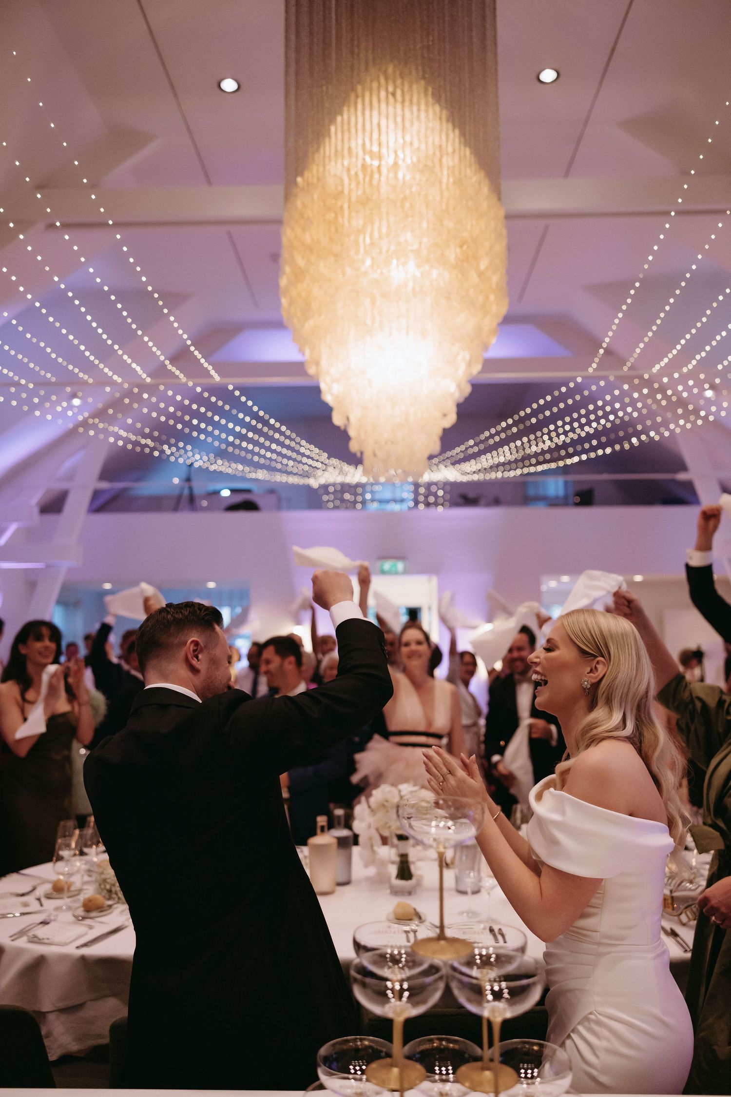 Elegant wedding reception hall with sparkling chandeliers and string lights creating a romantic atmosphere.