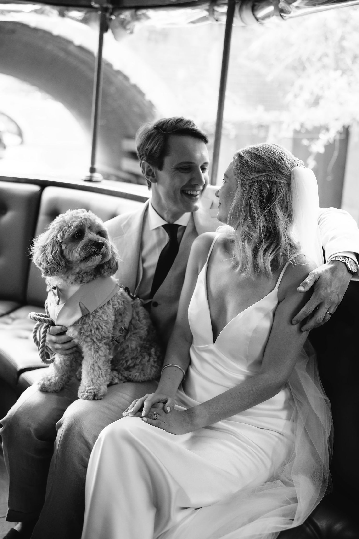Black and white photo of newlyweds with small dog in vintage car.