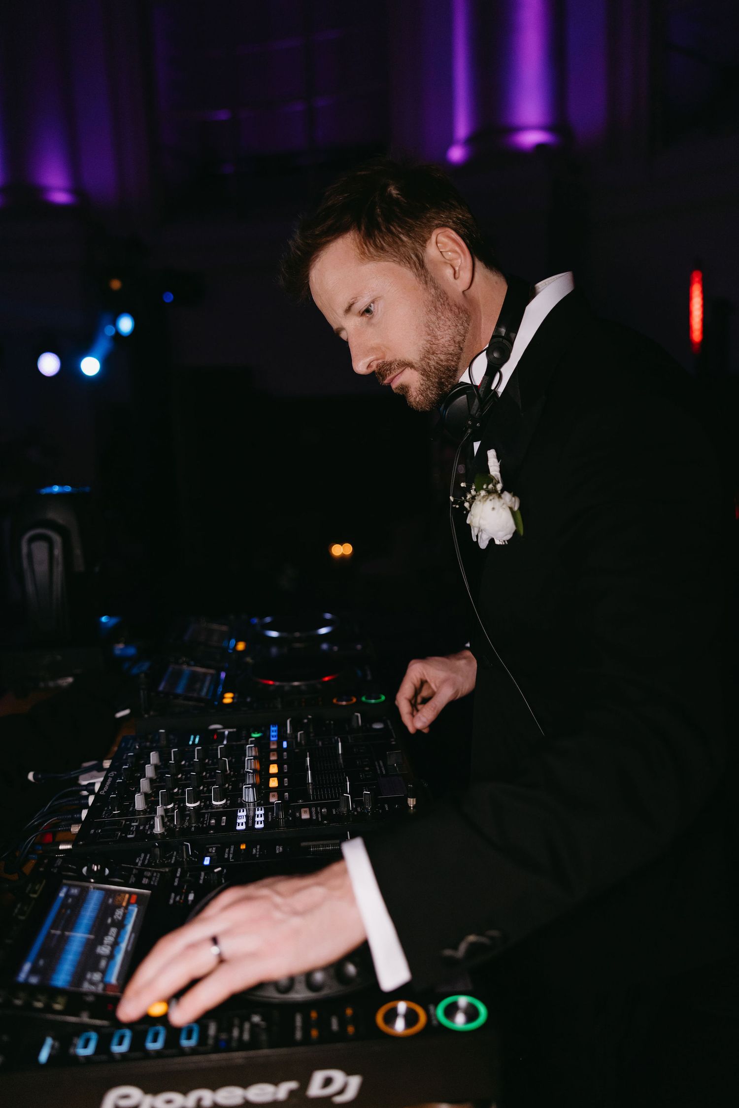 DJ in formal attire mixing music at wedding reception with professional equipment.