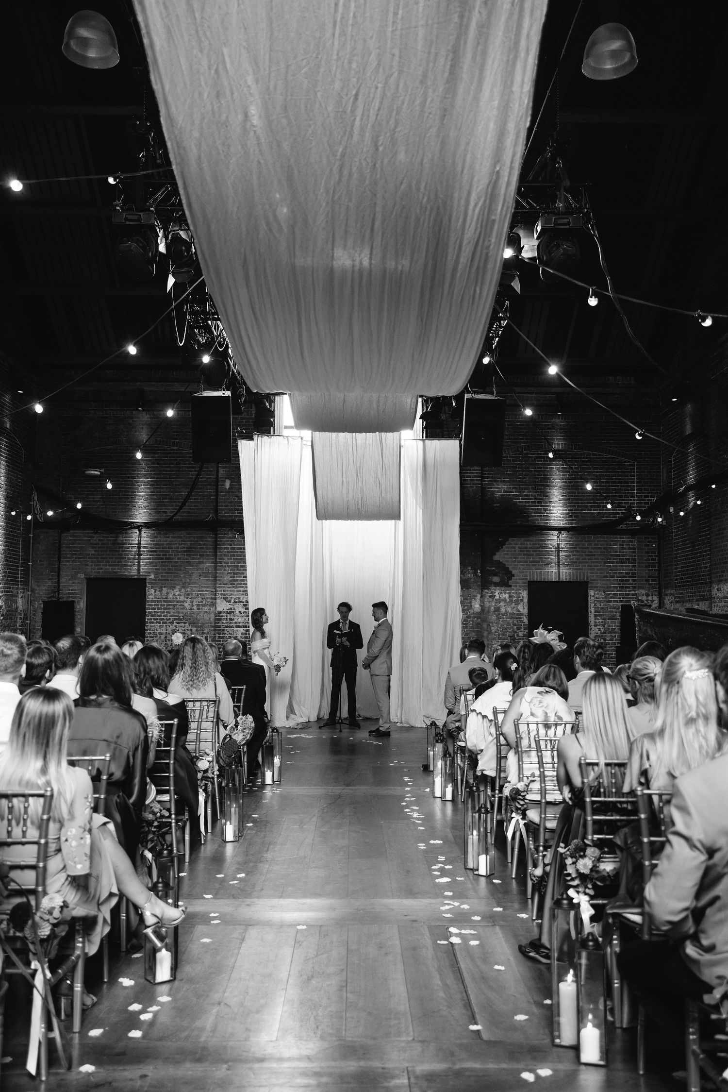 Wedding ceremony venue with white draped fabric and string lights creating an elegant indoor aisle.