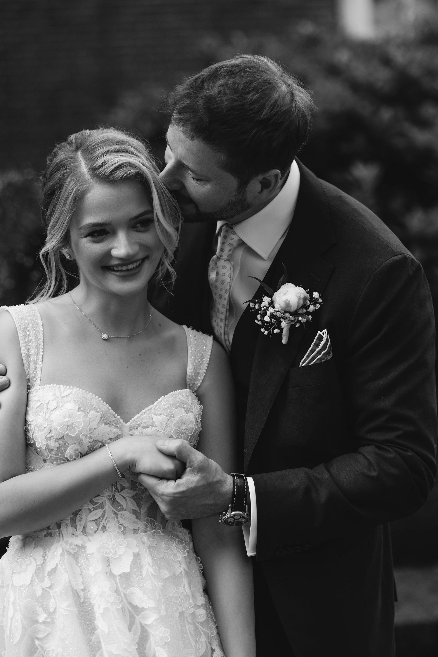 A tender newlywed moment between bride in lace dress and groom in black suit.