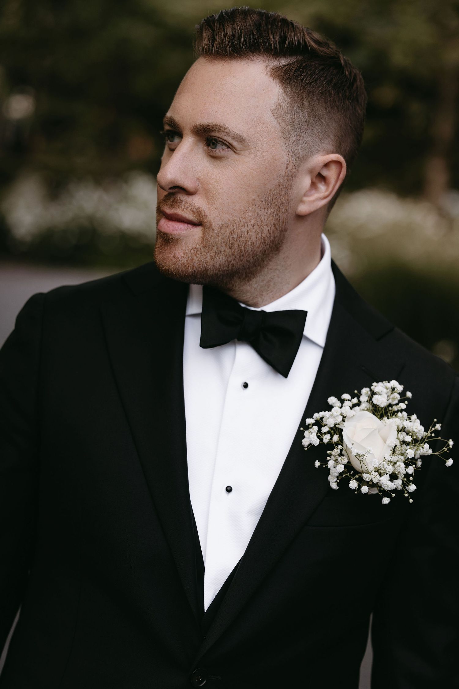 Classic groom portrait in black tuxedo with white boutonniere and bow tie.