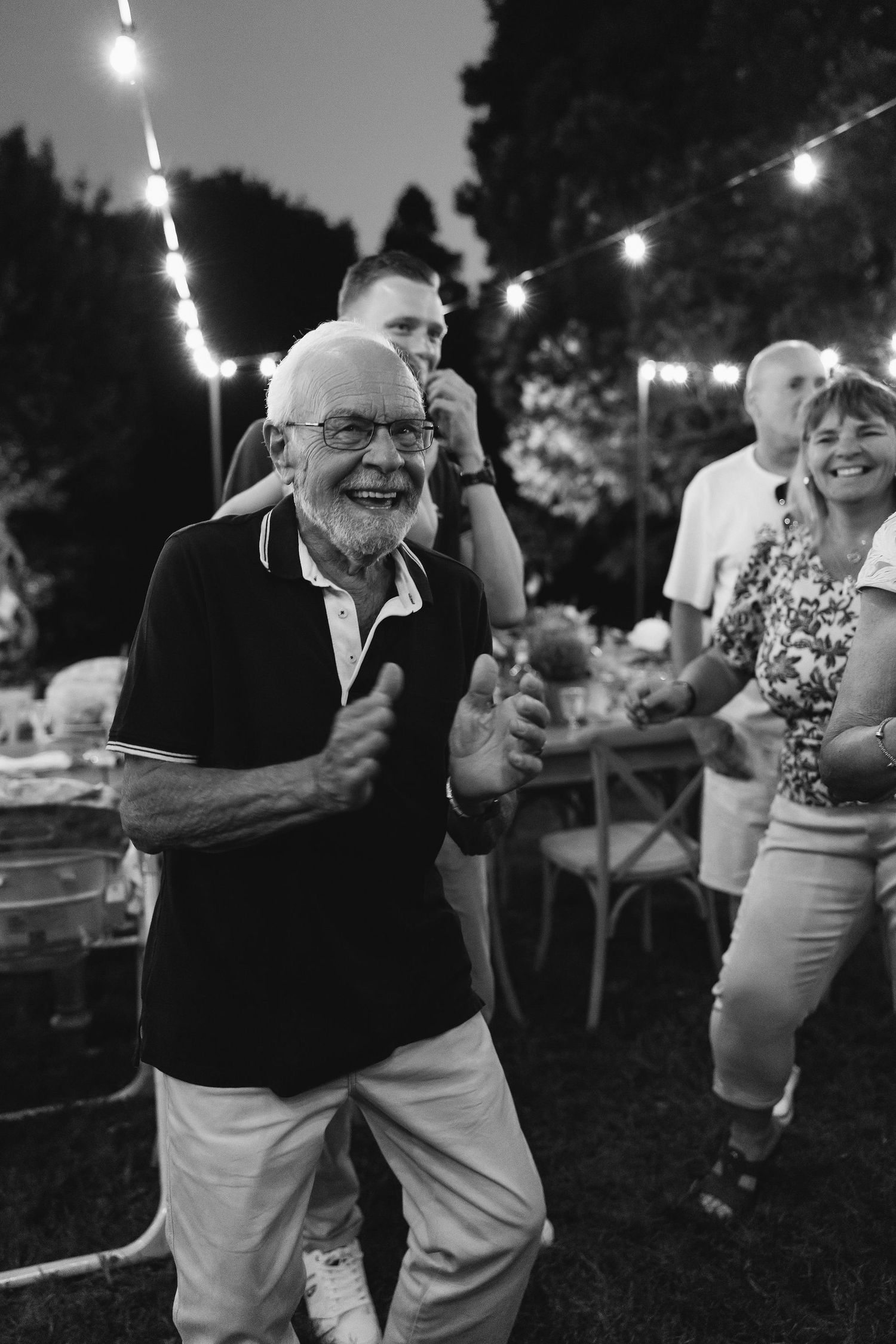 People dancing at an outdoor wedding reception with string lights overhead.
