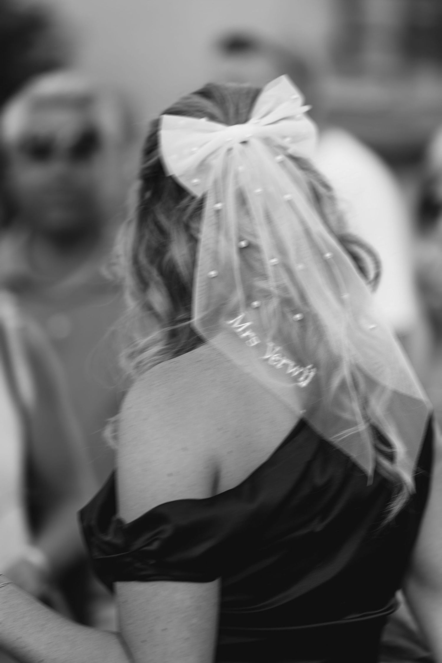 A black and white photo showing a white bow veil adorned with pearls on a wedding dress.